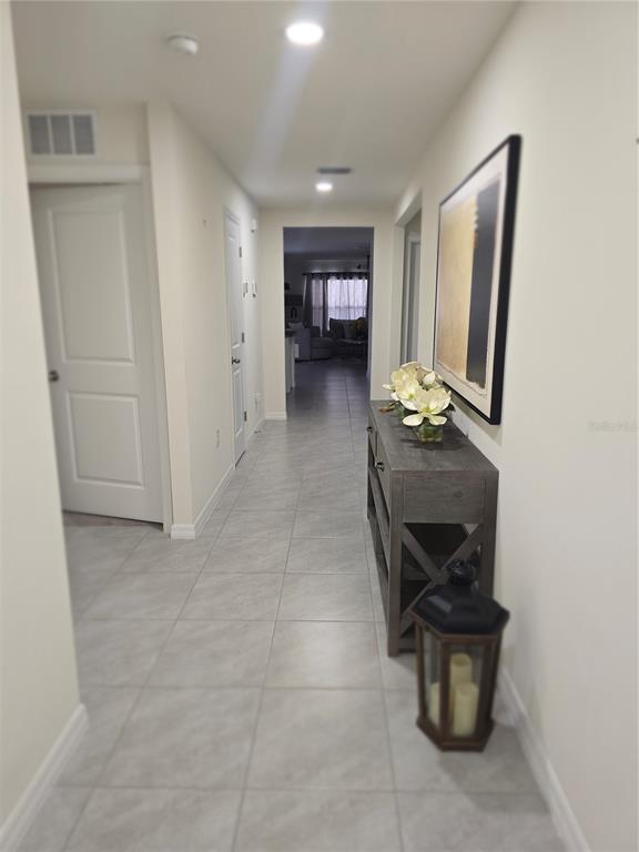 A hallway with light tile flooring leads toward a living area with a console table — 16706 SUNBURST LAKE STREET, WIMAUMA, FL