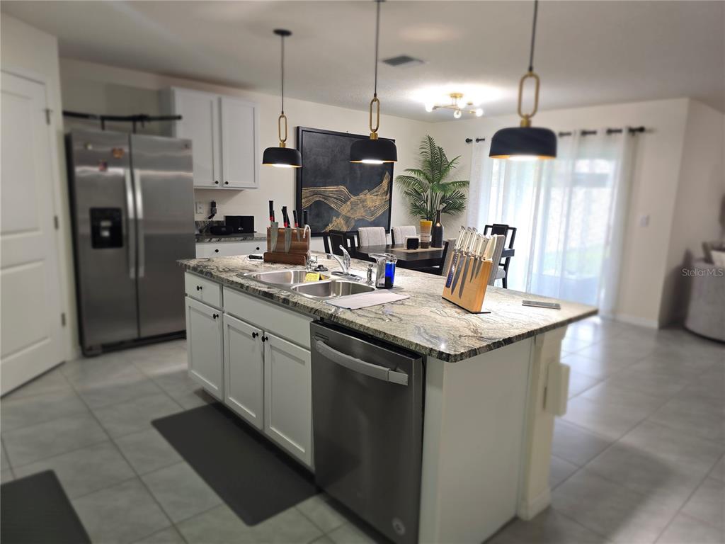 A kitchen features a granite-topped island with a stainless steel dishwasher and sink — 16706 SUNBURST LAKE STREET, WIMAUMA, FL
