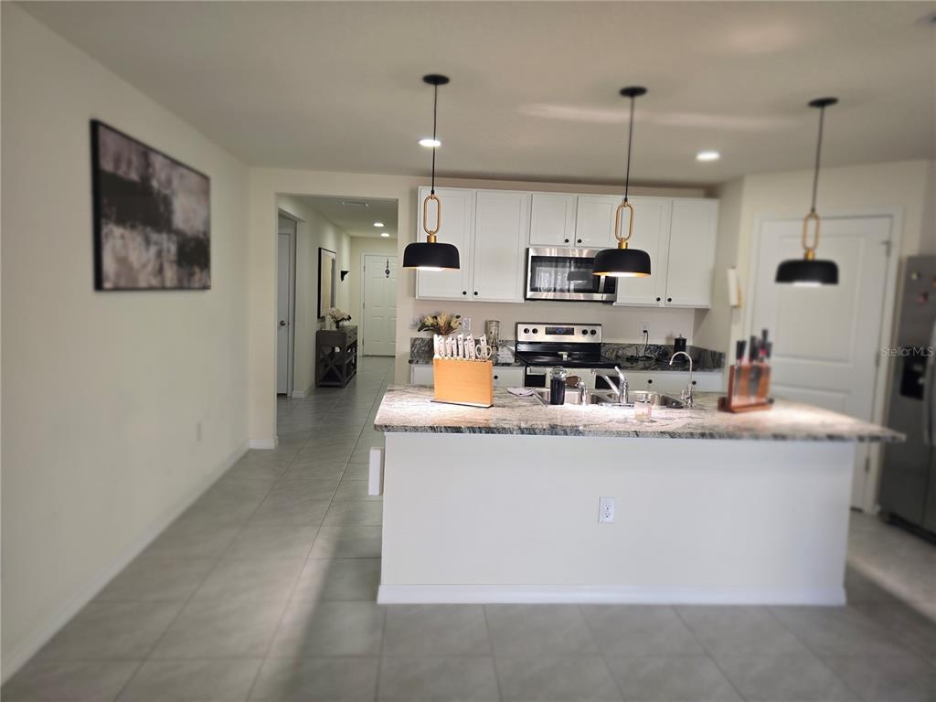A kitchen features white cabinets, granite countertops, a central island, and three pendant lights — 16706 SUNBURST LAKE STREET, WIMAUMA, FL