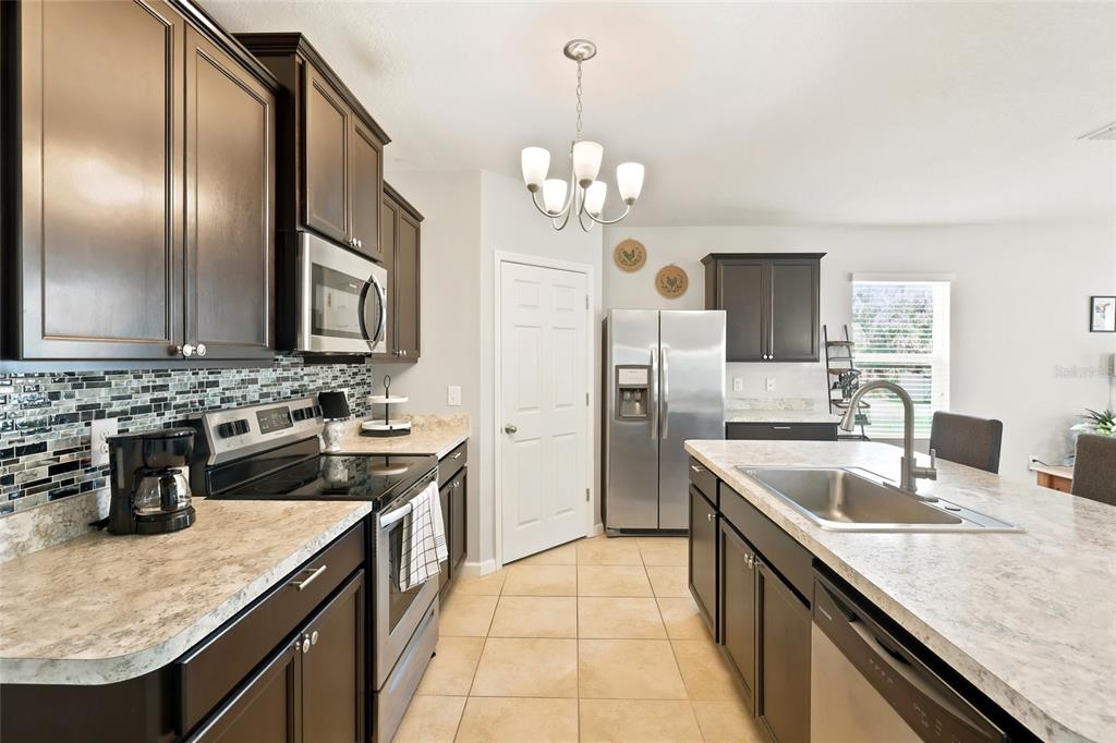 A kitchen features dark wood cabinets, stainless steel appliances, a center island, and tile flooring — 2096 SW LEAFY ROAD, PORT ST LUCIE, FL