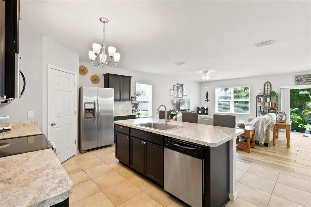 A kitchen with dark cabinets, stainless steel appliances, and an island overlooks a living area — 2096 SW LEAFY ROAD, PORT ST LUCIE, FL