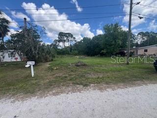 A vacant, grassy lot sits between two houses under a blue sky with clouds — 9320 CANAL ROAD, HAINES CITY, FL