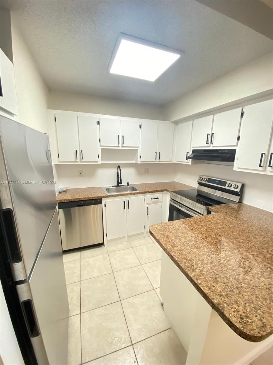 This kitchen features white cabinets, granite-look countertops, stainless steel appliances, and light tile flooring — 2029 NW 46th Ave # E308, Lauderhill FL 33313, LAUDERHILL, FL