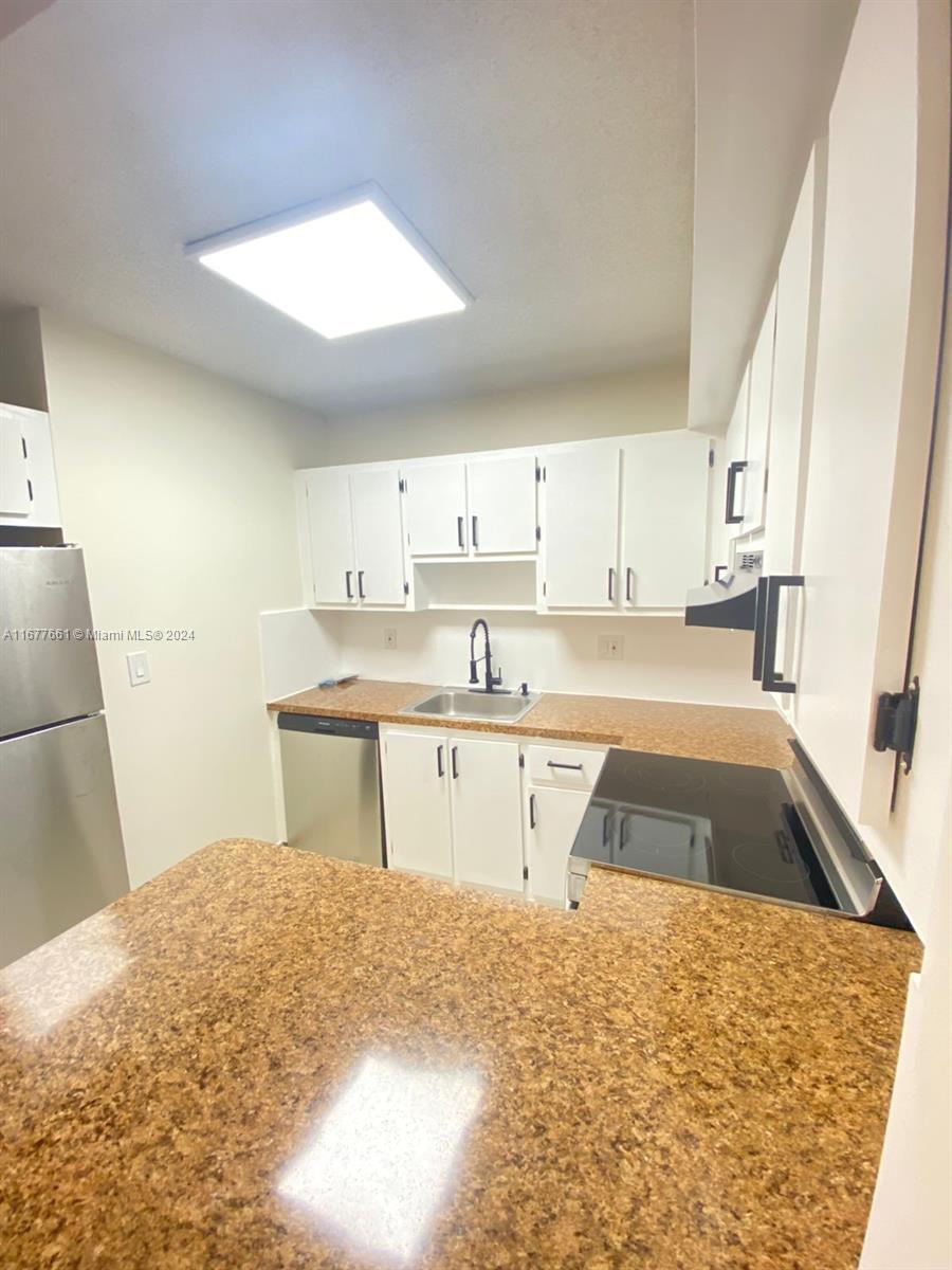 A kitchen features white cabinets, a stainless steel refrigerator, and speckled brown laminate countertops — 2029 NW 46th Ave # E308, Lauderhill FL 33313, LAUDERHILL, FL