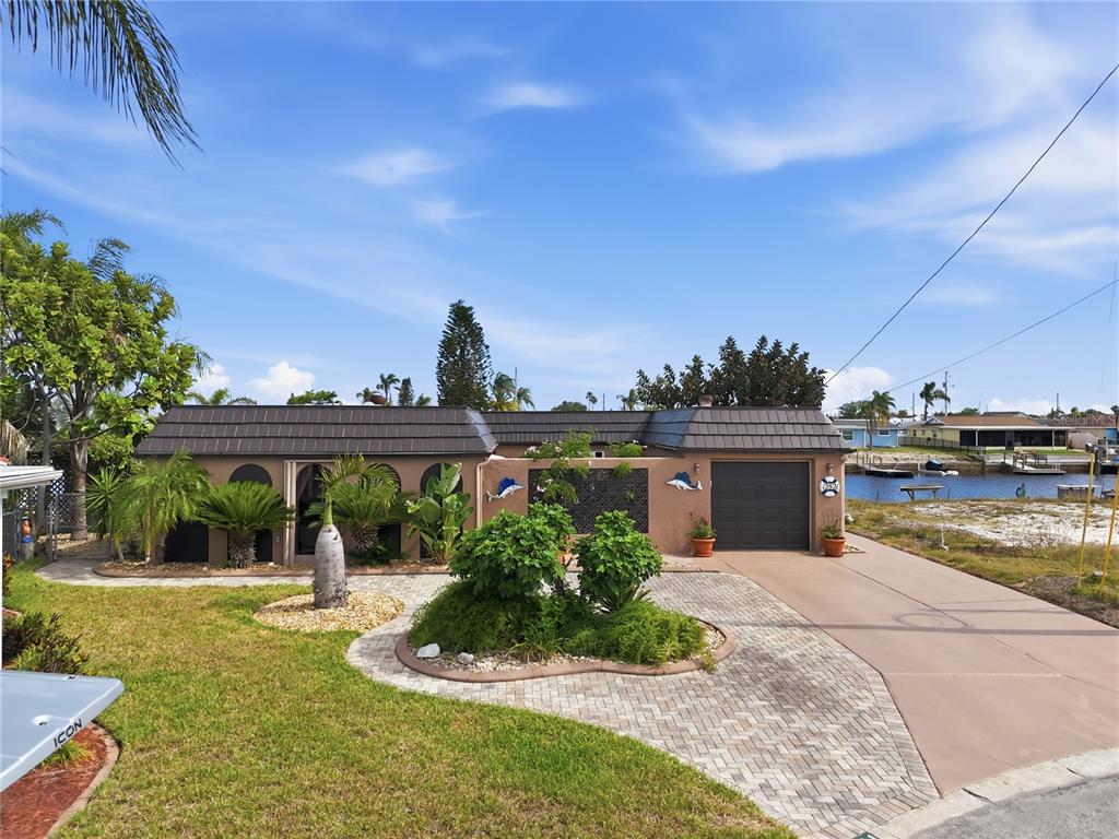 A single-story house with a dark tiled roof, tan stucco walls, and a paved driveway — 12821 4TH ISLE, HUDSON, FL