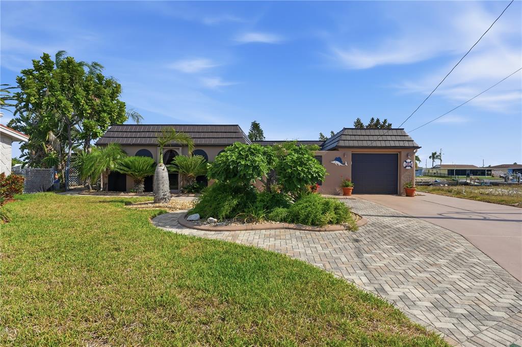 A single-story house with a dark mansard roof, a brick driveway, and lush landscaping — 12821 4TH ISLE, HUDSON, FL