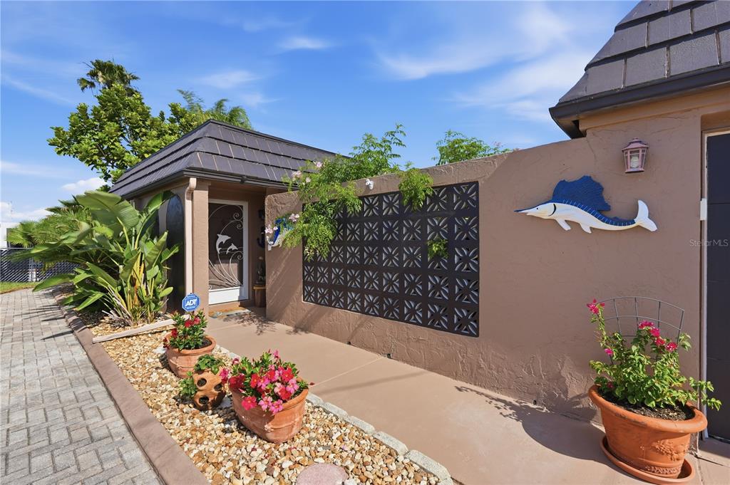 A paved walkway leads to a home entrance featuring a decorative screen wall and planters — 12821 4TH ISLE, HUDSON, FL