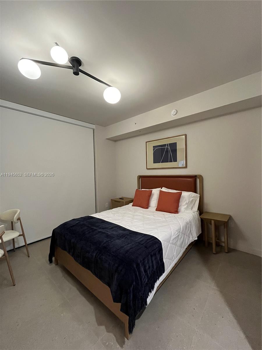 A bedroom features a bed with orange pillows, a dark throw, and a modern light fixture — 11 NE 6TH # 1006, Miami FL 33132, MIAMI, FL