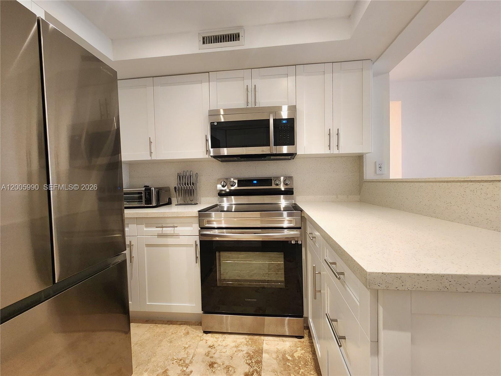 A kitchen features white cabinets, stainless steel appliances, and light-colored speckled countertops — 3505 S Ocean Dr # 209, Hollywood FL 33019, HOLLYWOOD, FL