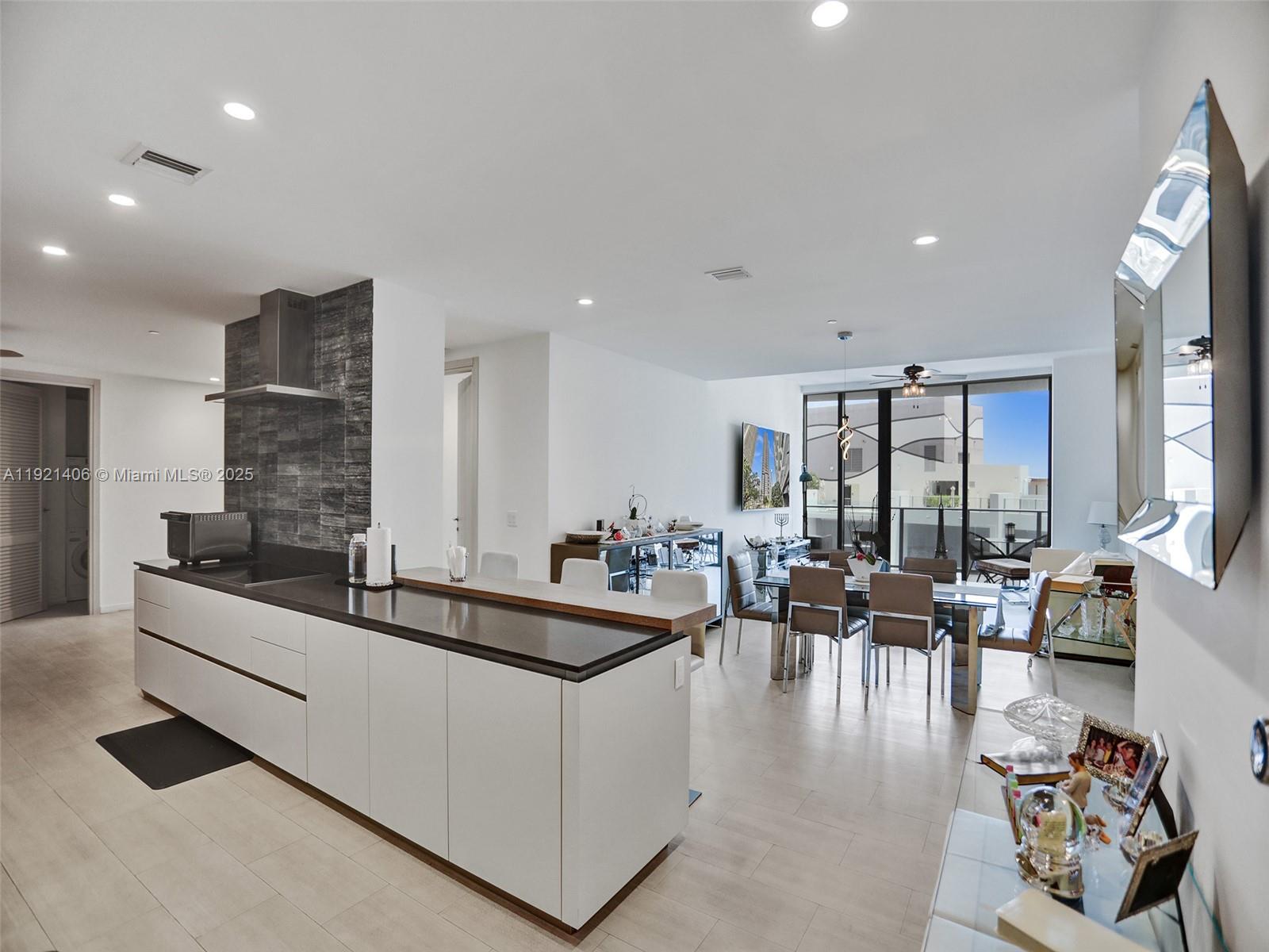 A modern open-concept kitchen and dining area features white cabinetry, dark countertops, and tile flooring — 1000 Brickell Plz, Miami FL 33131, MIAMI, FL