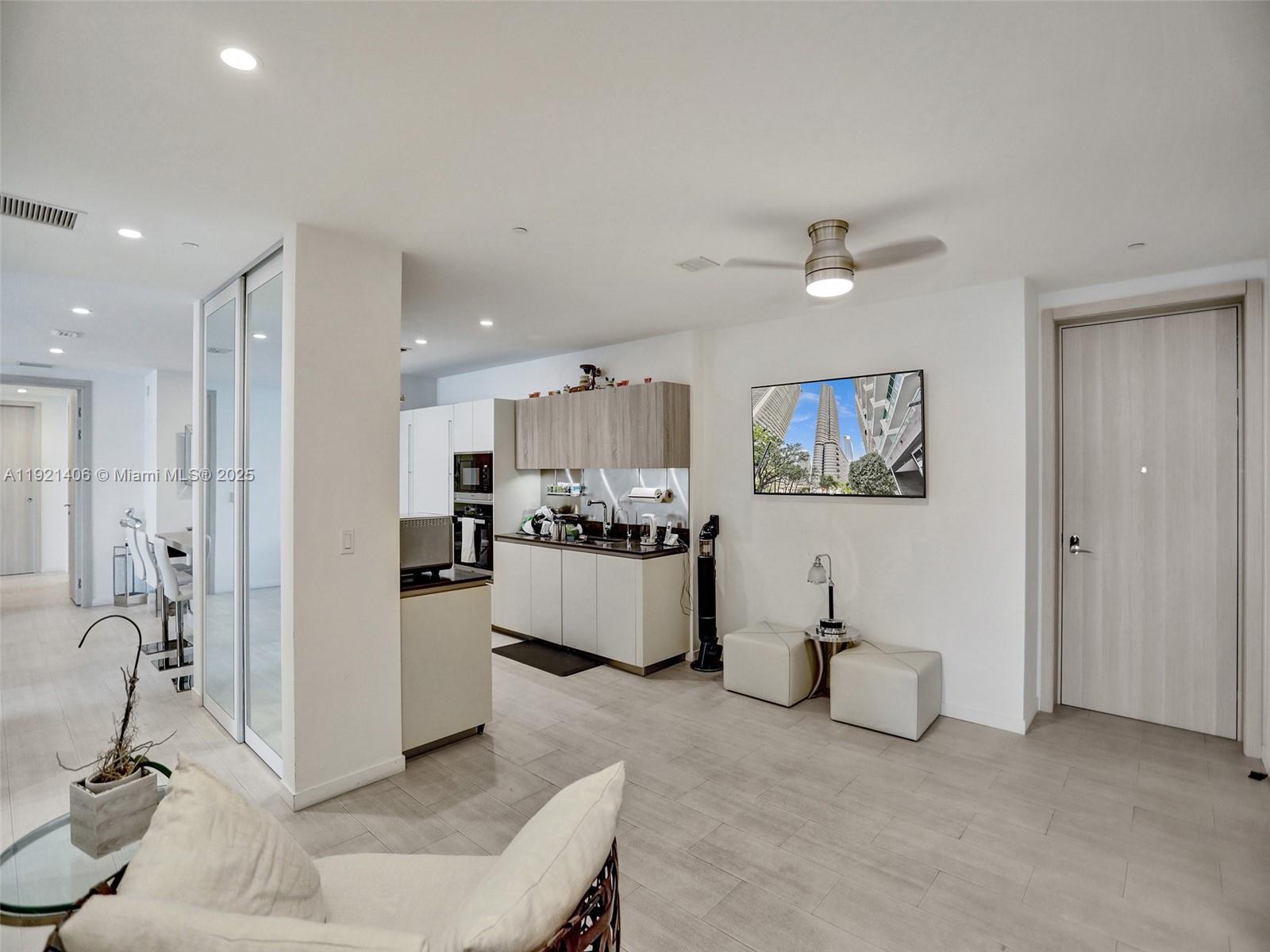 A modern kitchen with light cabinetry and a living area featuring a wall-mounted television — 1000 Brickell Plz, Miami FL 33131, MIAMI, FL