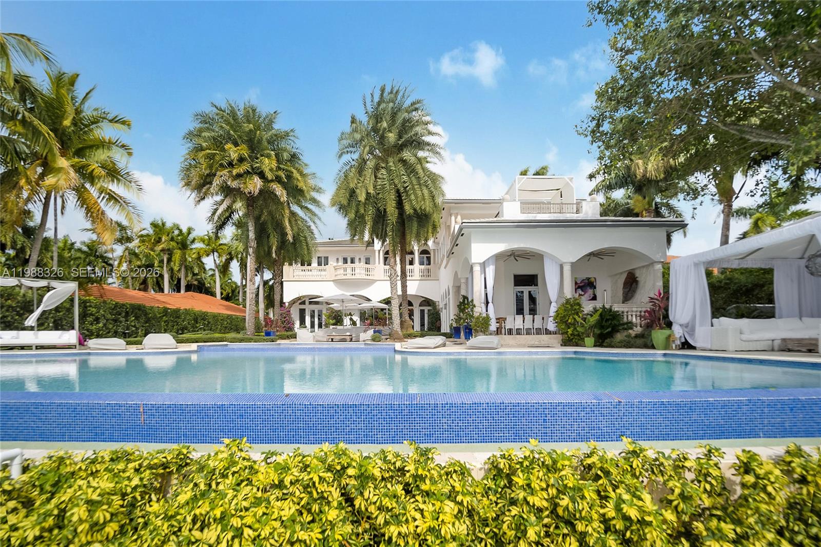 A swimming pool sits in front of a white two-story house with palm trees — 100 Palm Ave, Miami Beach FL 33139, MIAMI BEACH, FL