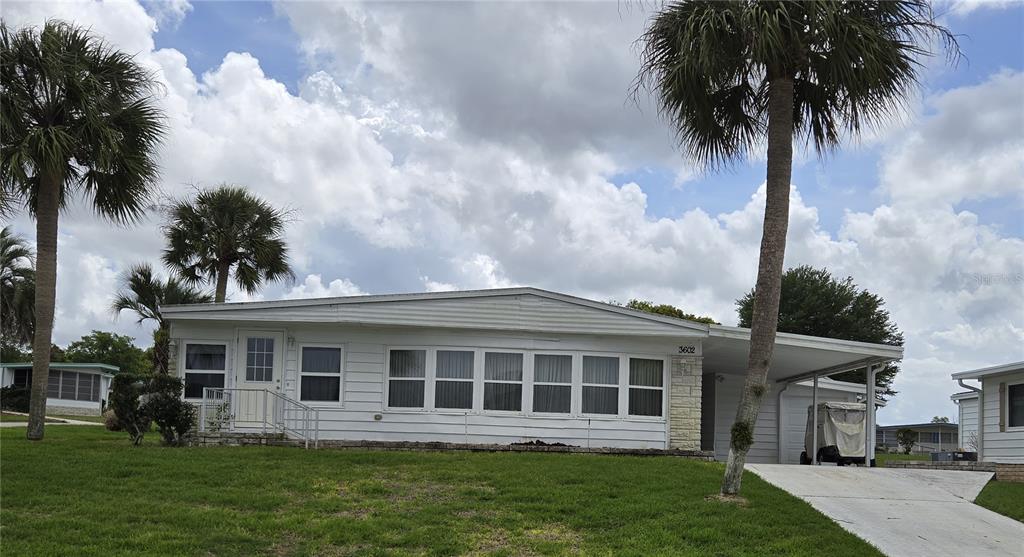 A white single-story manufactured home features a front carport, a paved driveway, and palm trees — 3602 N CITRUS CIRCLE UNIT 1529, ZELLWOOD, FL