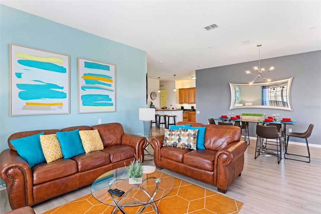 A living room with brown leather sofas, blue and yellow accents, and an adjacent dining area — 4840 CAYVIEW AVENUE UNIT 403, ORLANDO, FL