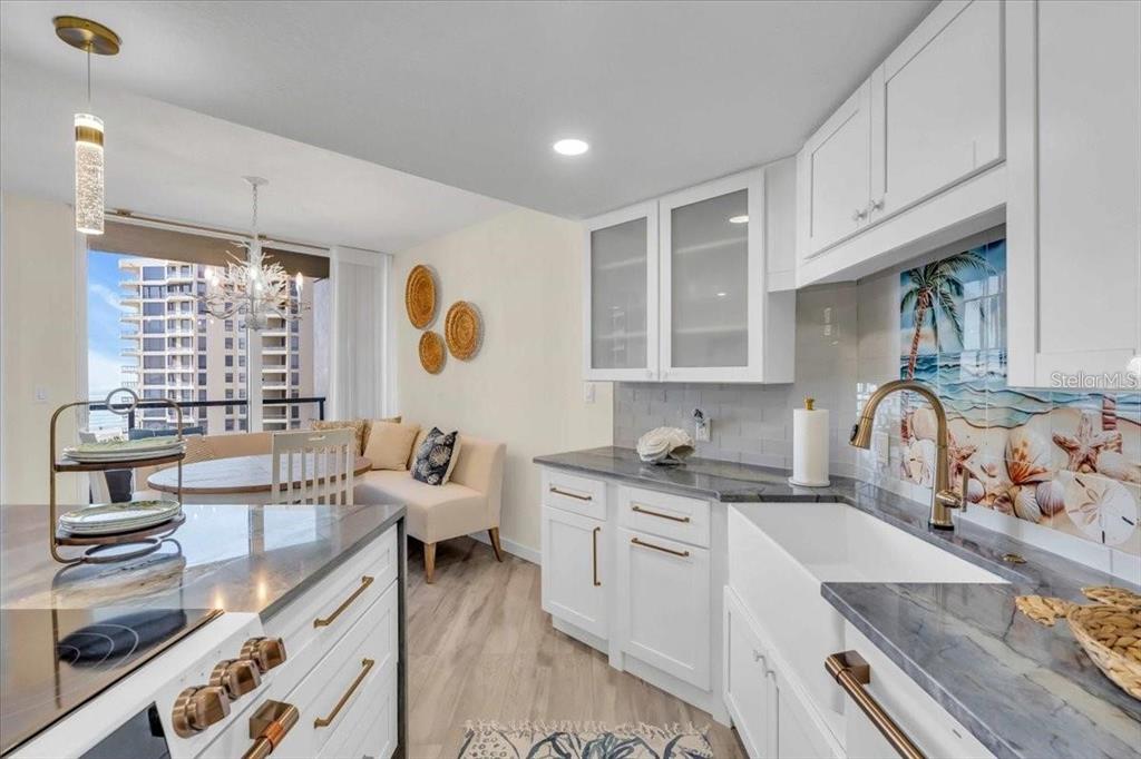 A bright kitchen features white cabinets, dark countertops, a farmhouse sink, and a dining area — 1211 GULF OF MEXICO DRIVE UNIT 403, LONGBOAT KEY, FL