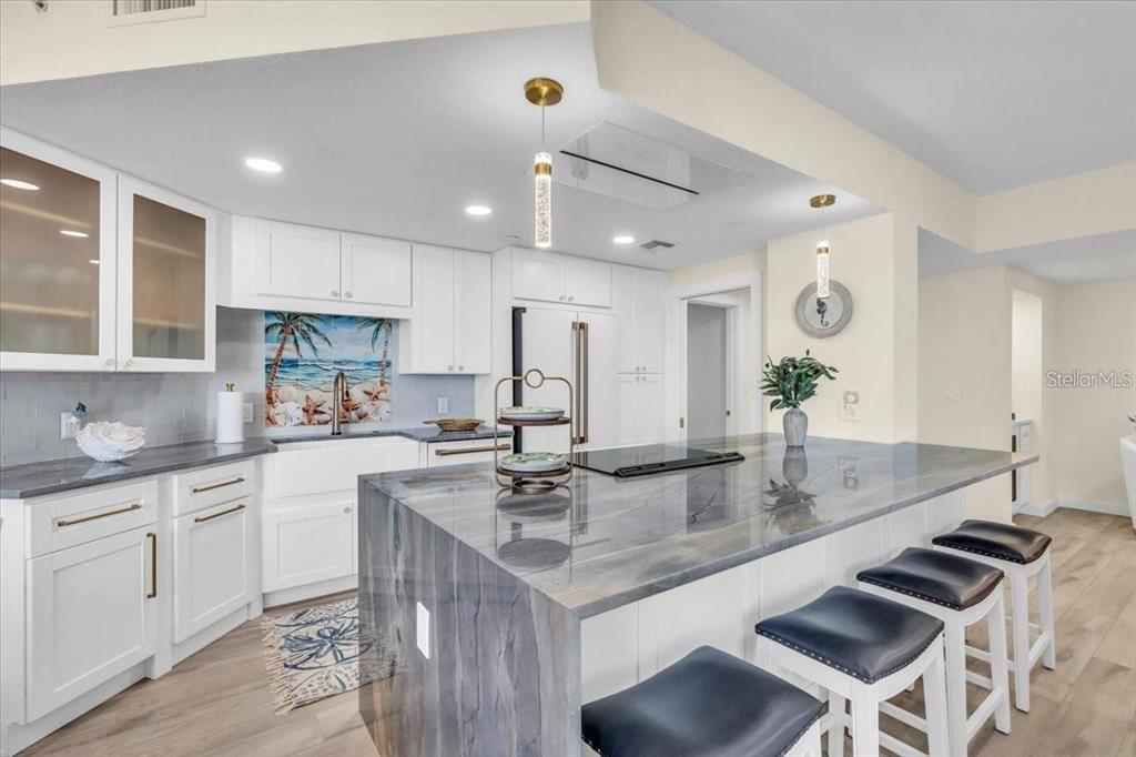 A modern kitchen features white cabinetry, a large gray stone island, and a beach-themed backsplash — 1211 GULF OF MEXICO DRIVE UNIT 403, LONGBOAT KEY, FL