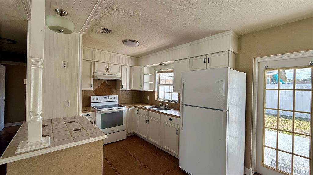 A kitchen features white cabinets, tile countertops, a white refrigerator, and a tiled floor — 1516 ALABAMA AVENUE, ST CLOUD, FL