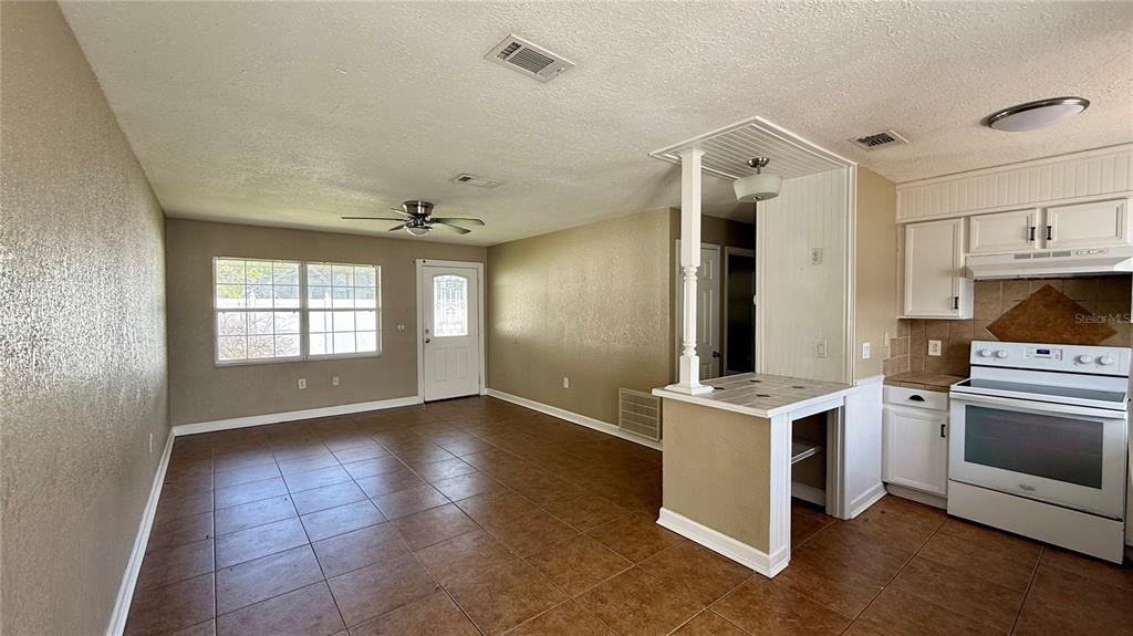An open-concept room features tile flooring, a kitchen with white cabinets, and a ceiling fan — 1516 ALABAMA AVENUE, ST CLOUD, FL