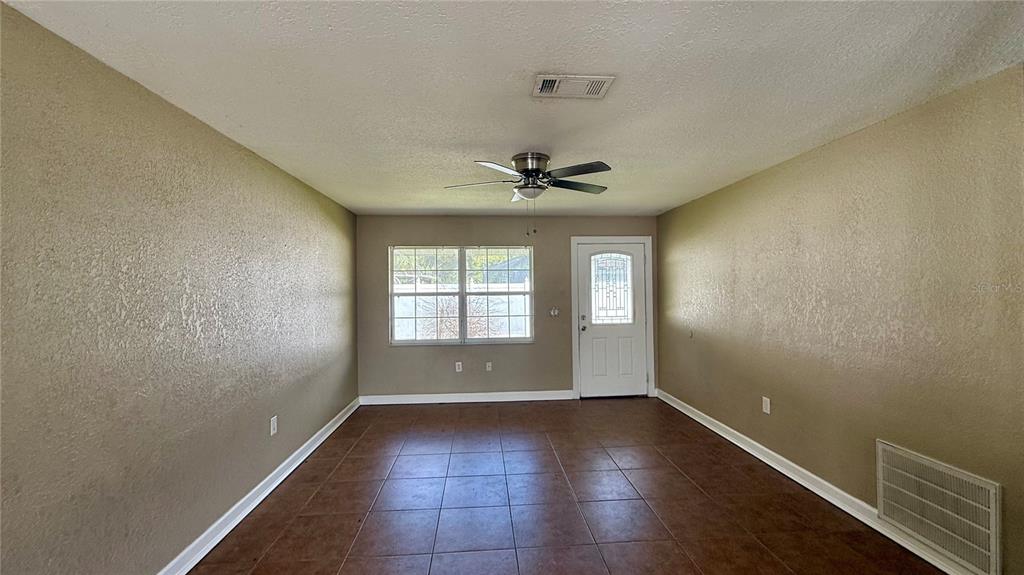 An empty room with tan walls, brown tile flooring, a ceiling fan, and a white door — 1516 ALABAMA AVENUE, ST CLOUD, FL