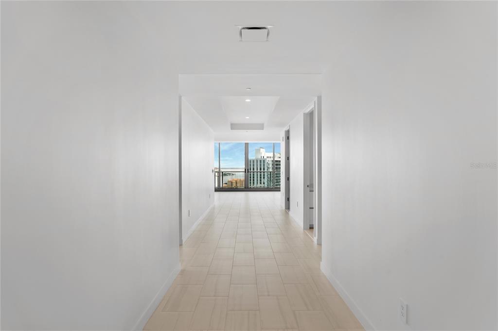 A long, white-walled hallway with light tile flooring leads toward a windowed living area — 400 CENTRAL AVENUE UNIT 3107, ST PETERSBURG, FL