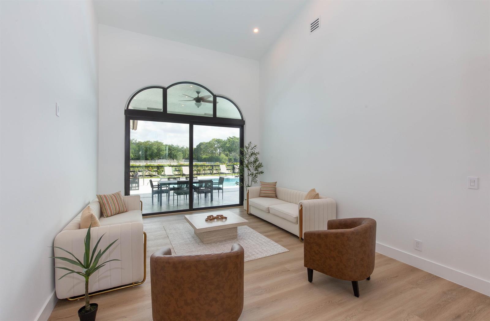 A bright living room features two cream sofas, two brown armchairs, and a sliding glass door — 14367 Belmont Trace, Wellington FL 33414, WELLINGTON, FL