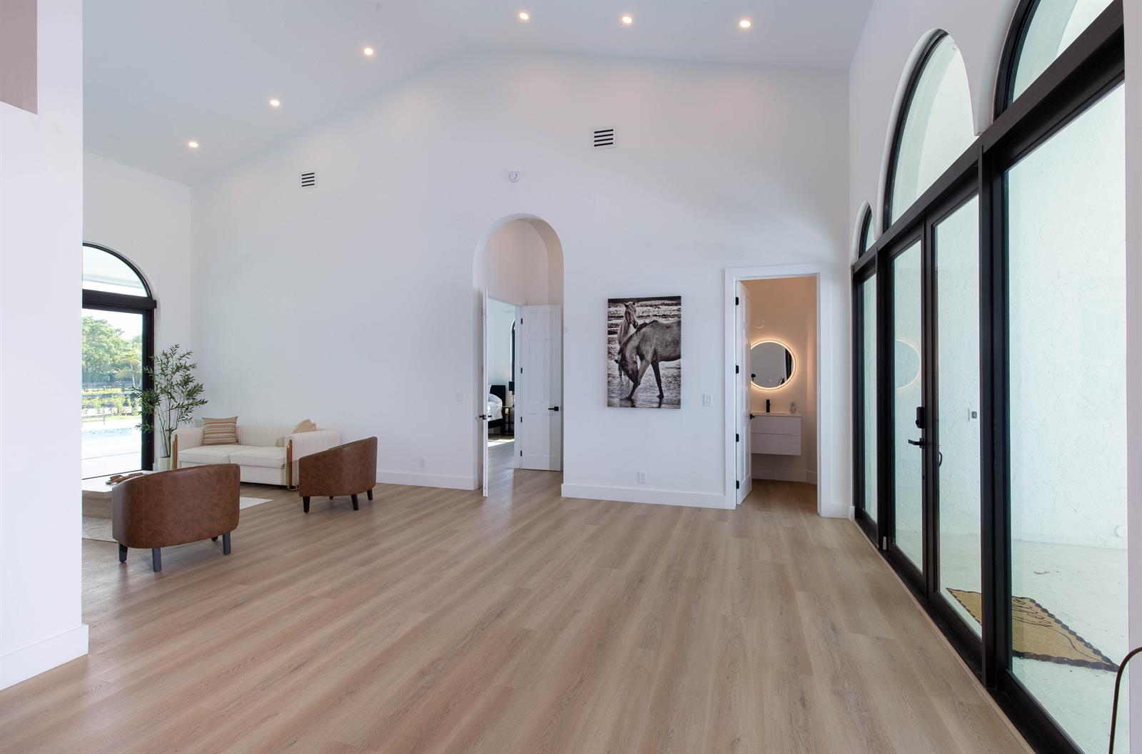 A bright, minimalist living room features white walls, light wood flooring, and large arched windows — 14367 Belmont Trace, Wellington FL 33414, WELLINGTON, FL