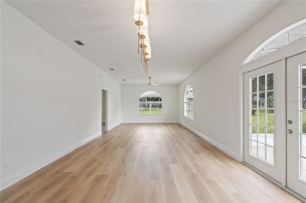An empty room with light wood flooring, white walls, arched windows, and a linear chandelier — 5619 PRINCE ANDREW COURT, LEESBURG, FL