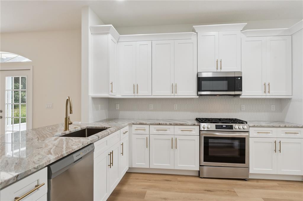 A kitchen with white cabinets, stainless steel appliances, and light wood flooring in a dining area — 5619 PRINCE ANDREW COURT, LEESBURG, FL