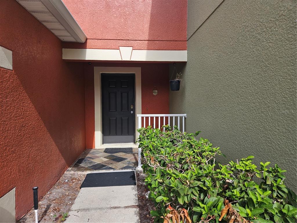 A front entrance with a dark door, tiled porch, and a green hedge — 752 CRESTING OAK CIRCLE UNIT 64, ORLANDO, FL