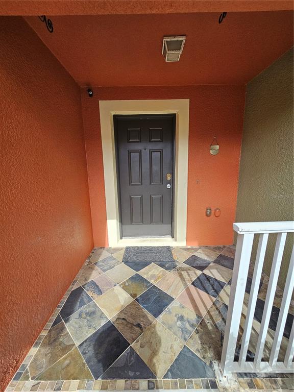 A front entryway features a dark door, orange stucco walls, and multi-colored slate tile flooring — 752 CRESTING OAK CIRCLE UNIT 64, ORLANDO, FL