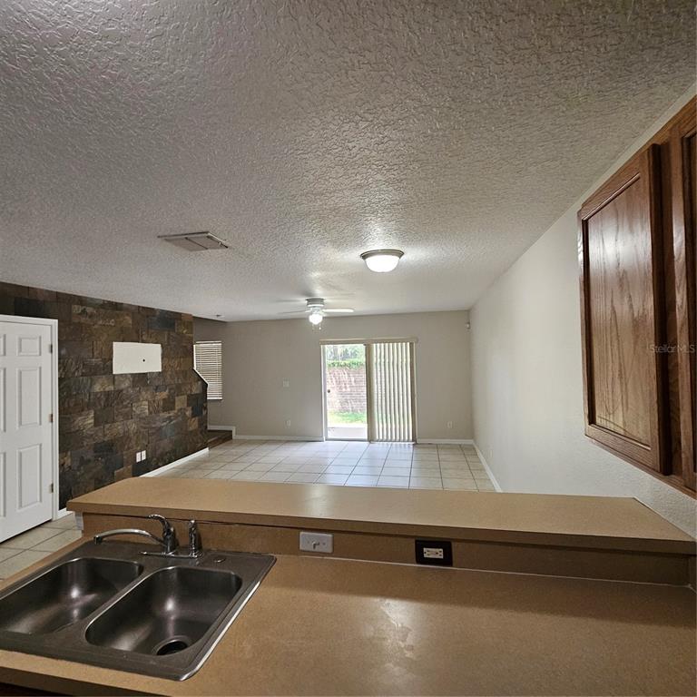 A kitchen sink overlooks a living area with tile flooring and a stone accent wall — 752 CRESTING OAK CIRCLE UNIT 64, ORLANDO, FL