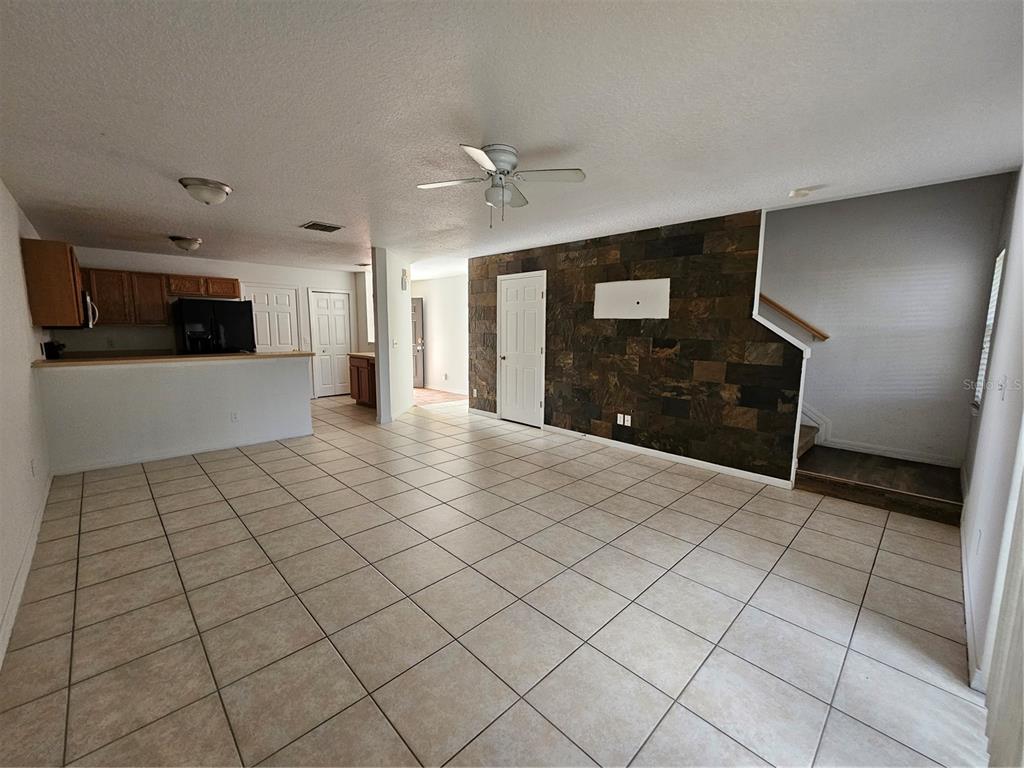An open-concept living area features light tile flooring, a stone accent wall, and a kitchen — 752 CRESTING OAK CIRCLE UNIT 64, ORLANDO, FL