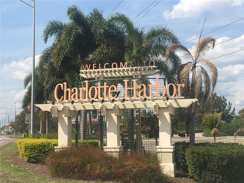 A decorative welcome sign for Charlotte Harbor stands outdoors surrounded by palm trees and landscaping — 2083 PORPOISE DRIVE, PUNTA GORDA, FL