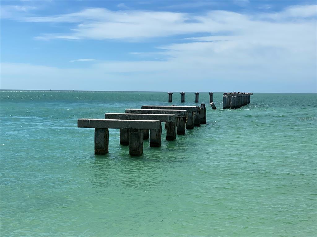 Concrete pilings from a ruined pier extend into the turquoise ocean under a blue sky — 2083 PORPOISE DRIVE, PUNTA GORDA, FL