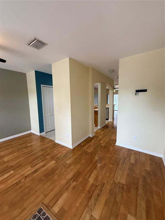 A room with hardwood flooring, light-colored walls, and an arched entryway leading to a kitchen — 15625 STABLE RUN DRIVE, SPRING HILL, FL