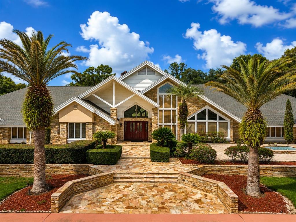 A stone-clad house with a gabled roof, arched front doors, and two palm trees — 1041 SWEETWATER CLUB BOULEVARD, LONGWOOD, FL