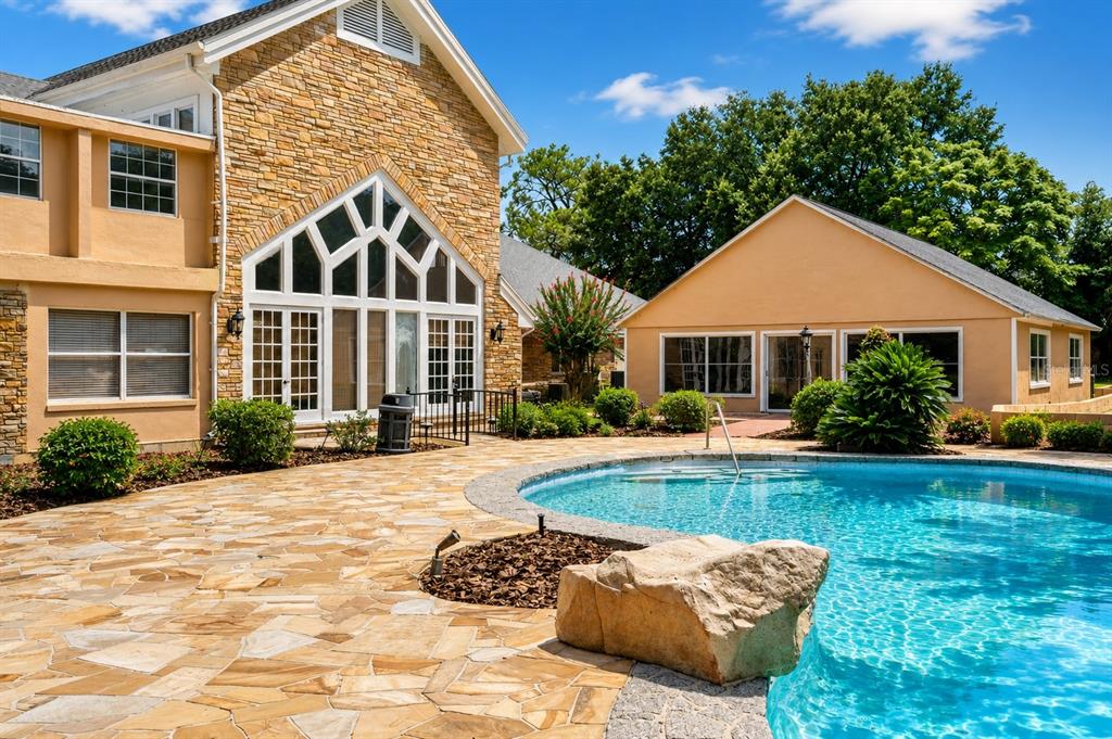A stone-paved pool deck sits in front of a large house with a stone facade — 1041 SWEETWATER CLUB BOULEVARD, LONGWOOD, FL