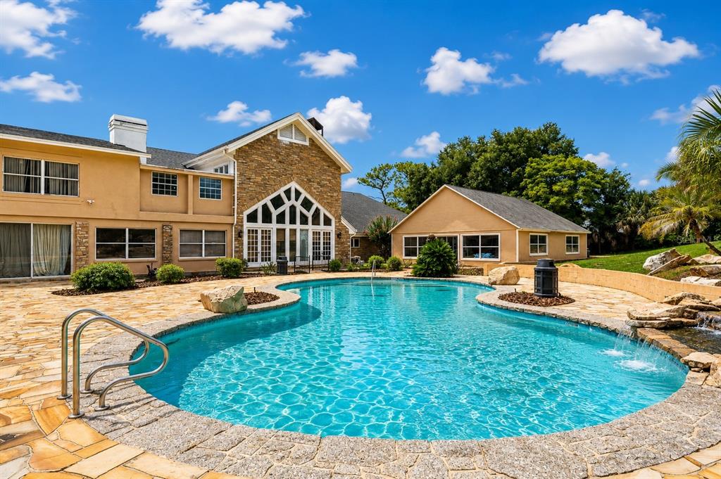 A stone-paved patio surrounds a swimming pool in front of a multi-story house — 1041 SWEETWATER CLUB BOULEVARD, LONGWOOD, FL