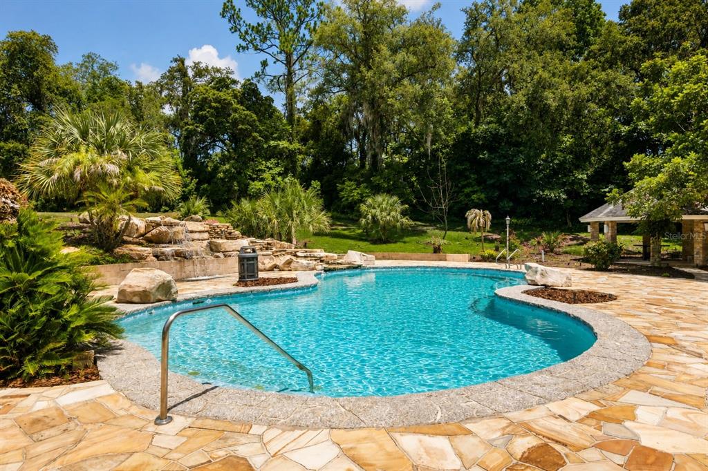 A backyard swimming pool with a rock waterfall feature and a stone patio — 1041 SWEETWATER CLUB BOULEVARD, LONGWOOD, FL
