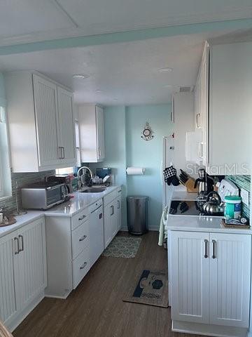 A galley-style kitchen features white beadboard cabinetry, light blue walls, and wood-look flooring — 1255 TARPON CENTER DRIVE UNIT 304, VENICE, FL