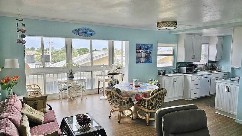 A light blue living and dining area features a round table, wicker chairs, and kitchen cabinetry — 1255 TARPON CENTER DRIVE UNIT 304, VENICE, FL