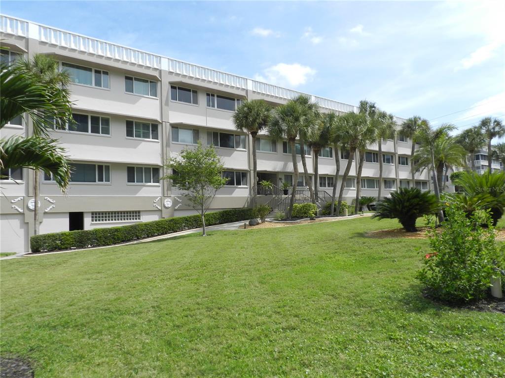 A multi-story apartment building with a lawn, palm trees, and landscaping in the foreground — 100 BLUFF VIEW DRIVE UNIT 109B, BELLEAIR BLUFFS, FL