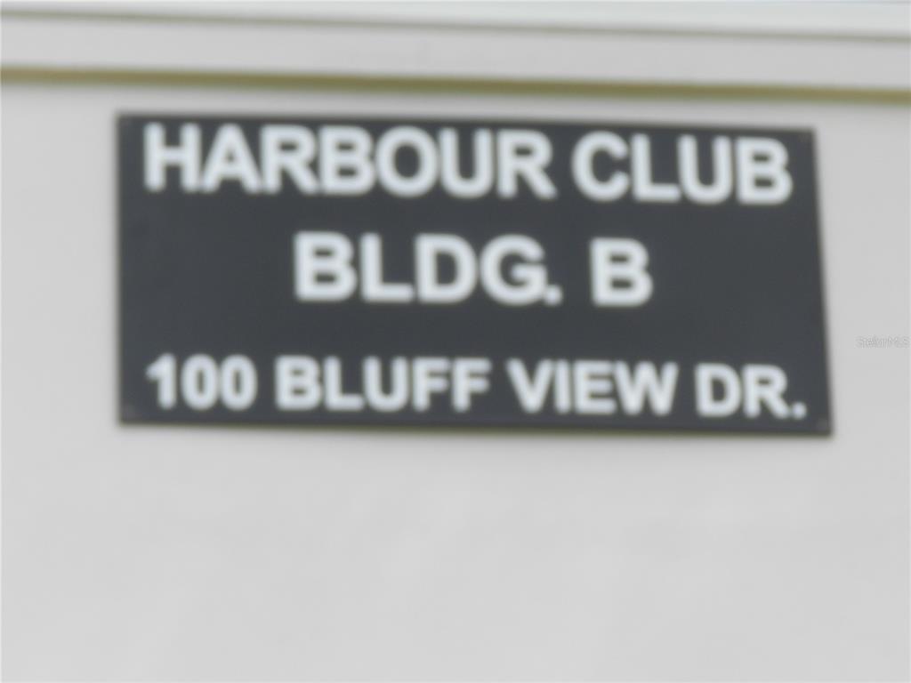 A black sign with white text identifies the building as Harbour Club Bldg. B — 100 BLUFF VIEW DRIVE UNIT 109B, BELLEAIR BLUFFS, FL