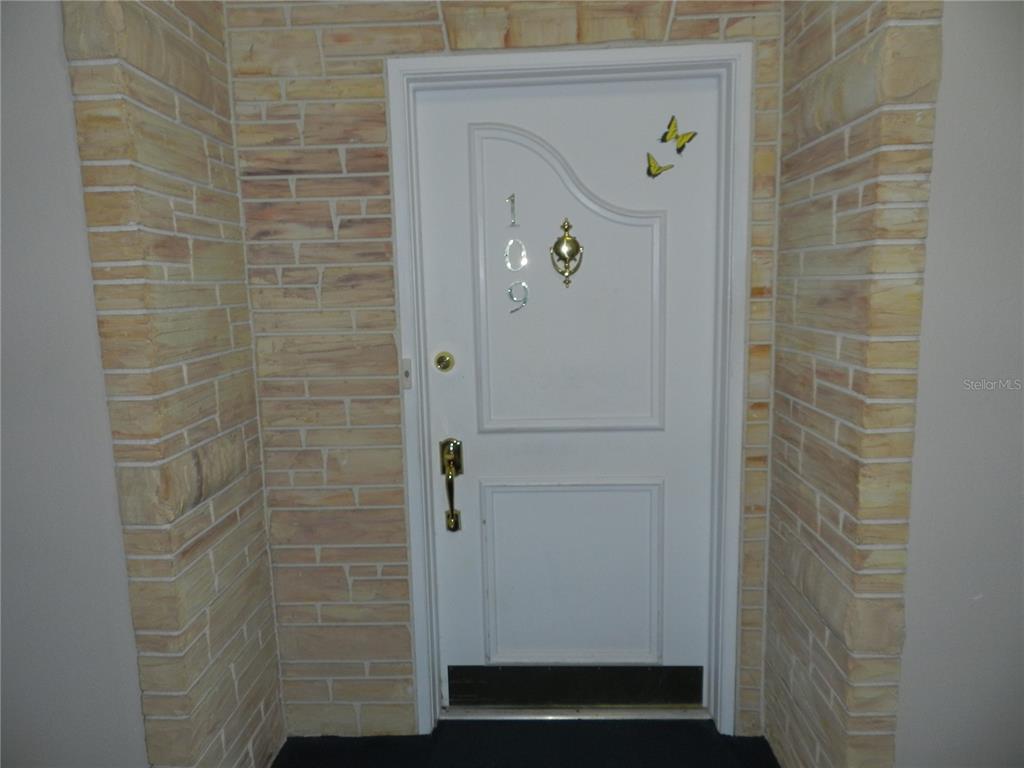 A white front door with a gold knocker and house numbers is set within a stone-clad entryway — 100 BLUFF VIEW DRIVE UNIT 109B, BELLEAIR BLUFFS, FL