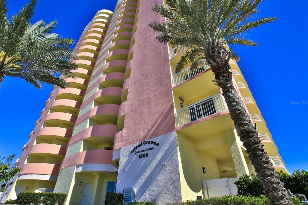 A low-angle view of a tall, pink, multi-story condominium building with curved balconies and palm trees — 1900 N ATLANTIC AVENUE UNIT 1603, DAYTONA BEACH, FL