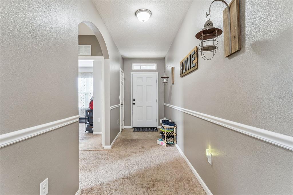 A carpeted entryway features a white front door, an arched doorway, and beige walls — 5617 YEARLING DRIVE, TITUSVILLE, FL