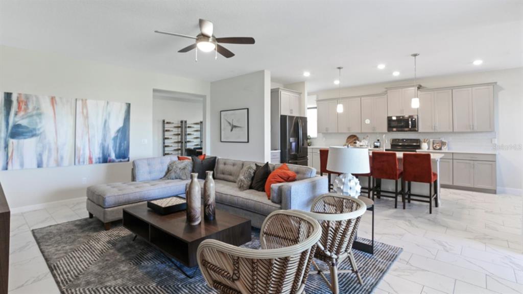 An open-concept living room and kitchen feature gray cabinetry, a sectional sofa, and tile flooring — 3156 NAMASTE DRIVE, CLERMONT, FL