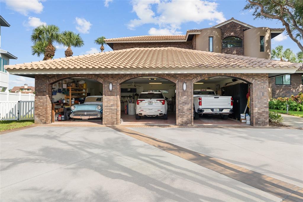A three-car garage with arched openings and a tiled roof attached to a brick house — 833 PONCE DE LEON DRIVE, TIERRA VERDE, FL