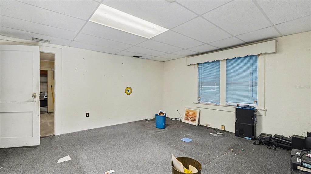 An empty room features a drop ceiling, gray carpeting, a window with blinds, and debris — 514 SW 2ND AVENUE, OCALA, FL