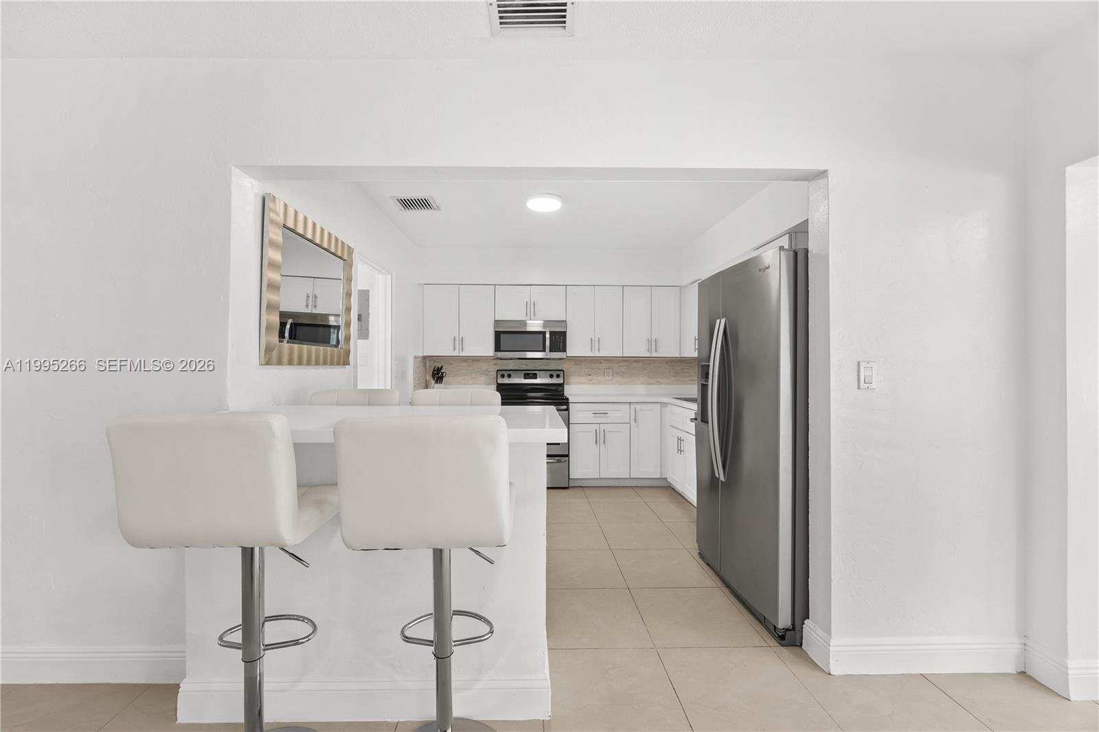 A kitchen features white cabinets, stainless steel appliances, and a breakfast bar with stools — 1435 Johnson St, Hollywood FL 33020, HOLLYWOOD, FL